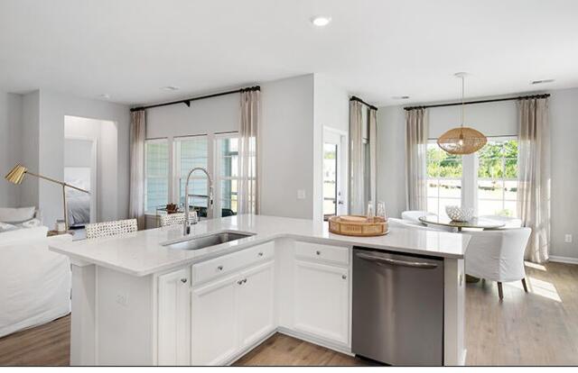 kitchen featuring sink, white cabinetry, dishwasher, decorative light fixtures, and a kitchen island with sink