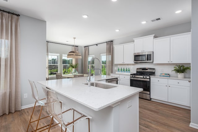 kitchen with white cabinetry, sink, stainless steel appliances, and a kitchen island with sink