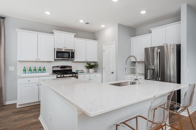 kitchen with stainless steel appliances, a kitchen bar, sink, white cabinetry, and a kitchen island with sink