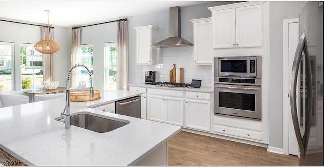 kitchen with appliances with stainless steel finishes, sink, wall chimney exhaust hood, and light stone counters