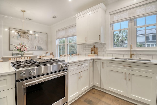 kitchen with stainless steel gas range oven, ornamental molding, a sink, white cabinetry, and backsplash