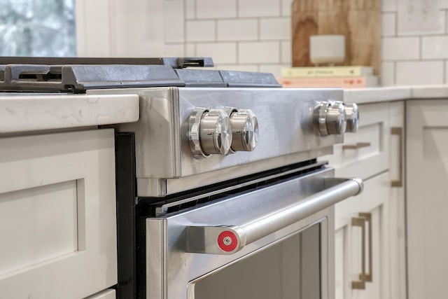 interior details featuring tile counters, gas stove, decorative backsplash, and white cabinets