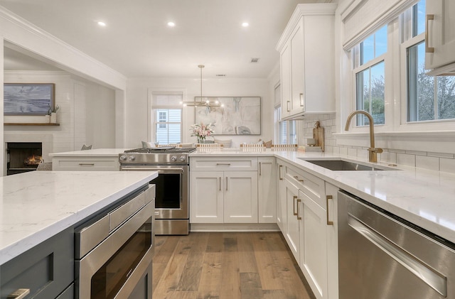 kitchen with a peninsula, a sink, stainless steel appliances, a lit fireplace, and dark wood-type flooring