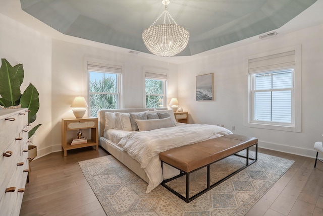 bedroom featuring a raised ceiling, multiple windows, an inviting chandelier, and visible vents