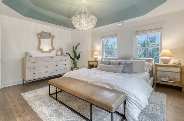 bedroom with a tray ceiling, a notable chandelier, hardwood / wood-style floors, and baseboards