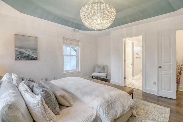 bedroom with an inviting chandelier, connected bathroom, wood finished floors, visible vents, and baseboards