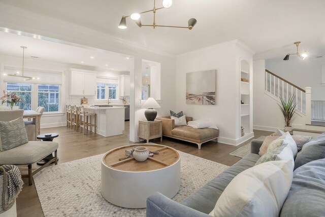 living area with stairs, ornamental molding, light wood finished floors, and an inviting chandelier