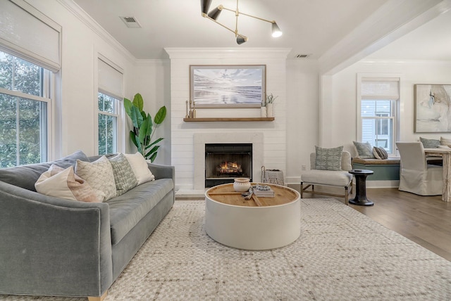 living area featuring crown molding, a large fireplace, visible vents, and wood finished floors