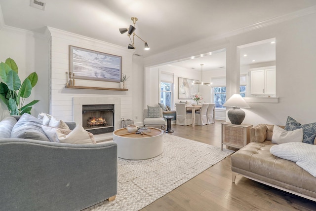 living area with crown molding, a warm lit fireplace, visible vents, and wood finished floors