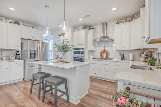 kitchen with appliances with stainless steel finishes, wall chimney exhaust hood, a sink, white cabinets, and recessed lighting