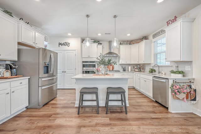 kitchen featuring wall chimney exhaust hood, stainless steel appliances, a sink, a center island, and white cabinets