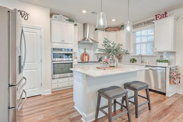 kitchen with appliances with stainless steel finishes, wall chimney range hood, light wood finished floors, white cabinets, and recessed lighting