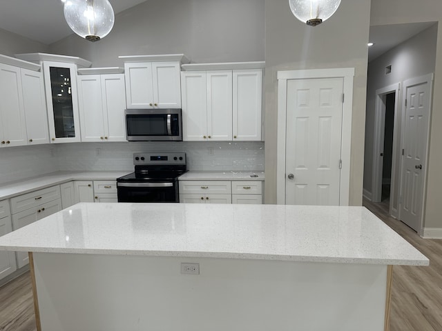 kitchen with a kitchen island, electric range oven, stainless steel microwave, white cabinetry, and tasteful backsplash