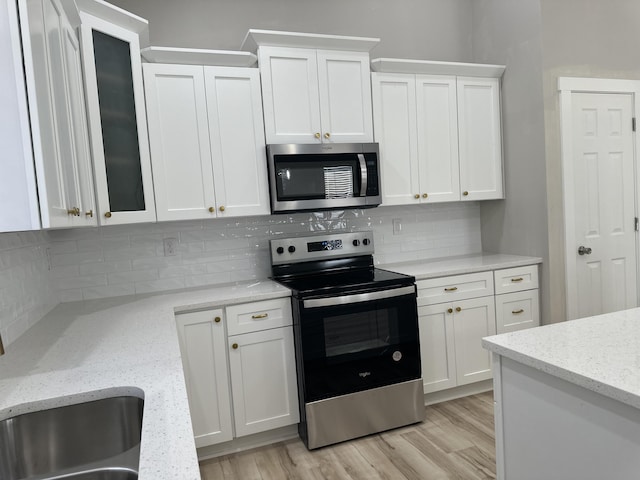 kitchen with white cabinets, stainless steel appliances, light wood-type flooring, and tasteful backsplash