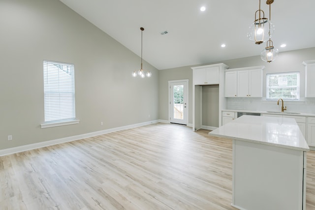 kitchen with a kitchen island, white cabinetry, a sink, high vaulted ceiling, and light wood-style flooring