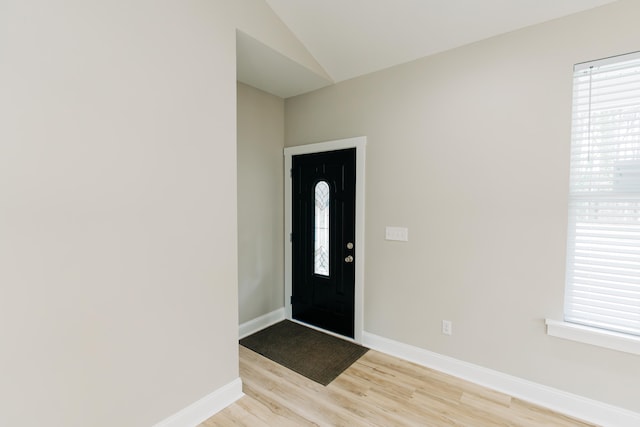 foyer with baseboards, light wood finished floors, and vaulted ceiling