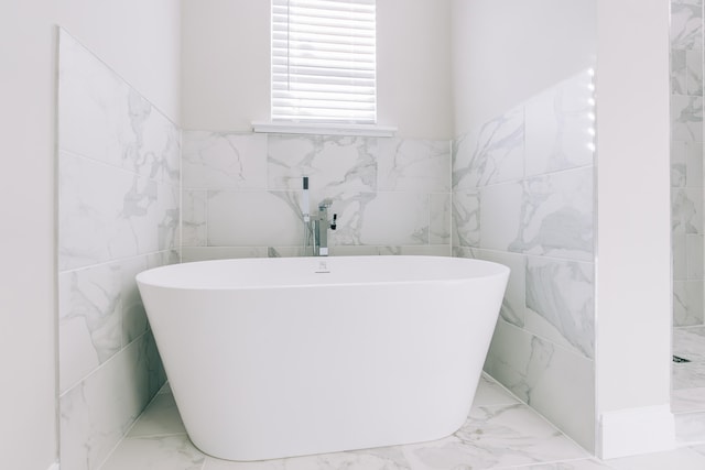 bathroom featuring tile walls, a soaking tub, a wainscoted wall, and marble finish floor