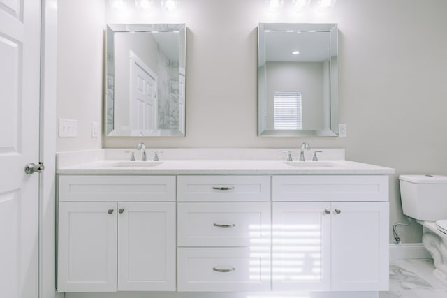 full bath with double vanity, a sink, marble finish floor, and toilet