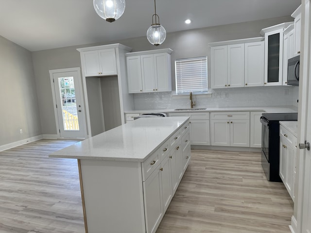 kitchen featuring decorative backsplash, a kitchen island, white cabinetry, a sink, and black appliances