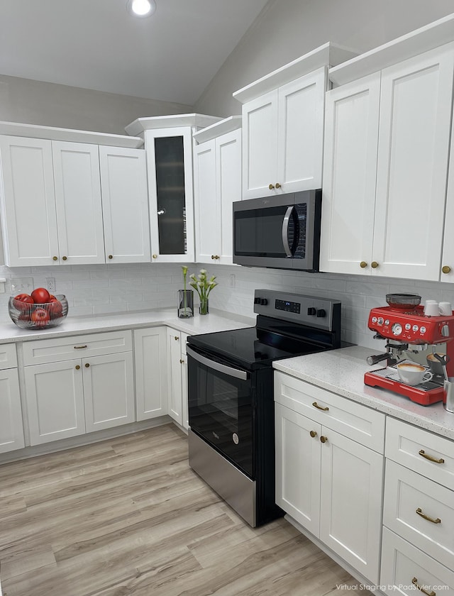 kitchen featuring appliances with stainless steel finishes, white cabinetry, decorative backsplash, lofted ceiling, and glass insert cabinets