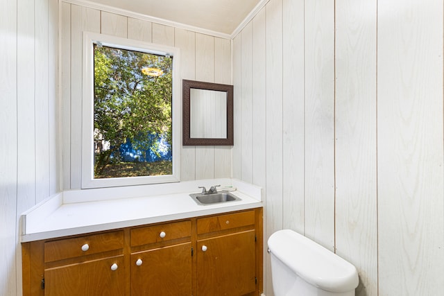 bathroom featuring ornamental molding, vanity, wooden walls, and toilet