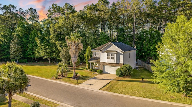 traditional-style home with an attached garage, a yard, driveway, and view of wooded area