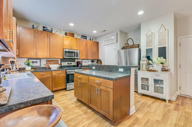 kitchen featuring appliances with stainless steel finishes, a sink, light wood-style flooring, dark countertops, and recessed lighting