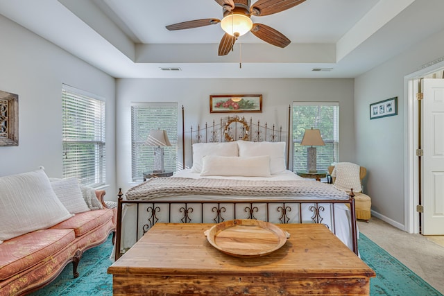 bedroom featuring a raised ceiling, light carpet, baseboards, and ceiling fan