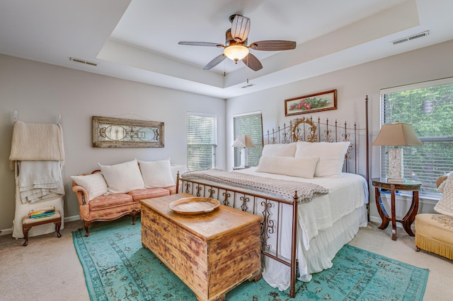 bedroom featuring light colored carpet, a raised ceiling, baseboards, and ceiling fan