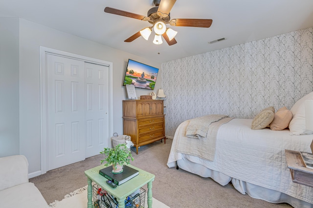 bedroom with carpet, a closet, wallpapered walls, a ceiling fan, and an accent wall
