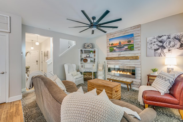 living room with wood finished floors, a ceiling fan, a fireplace, and baseboards