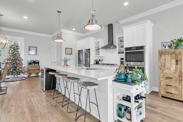 kitchen with sink, hanging light fixtures, wall chimney range hood, light hardwood / wood-style floors, and white cabinets