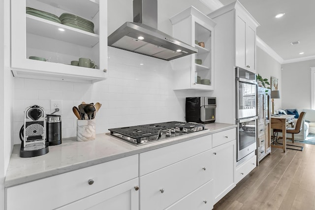 kitchen with light stone countertops, appliances with stainless steel finishes, wall chimney exhaust hood, light hardwood / wood-style flooring, and white cabinetry