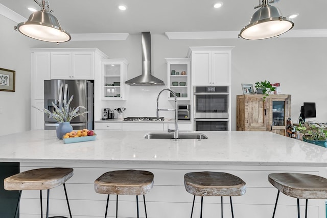 kitchen featuring a kitchen bar, white cabinets, stainless steel appliances, and wall chimney range hood