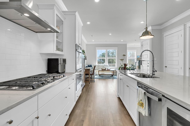 kitchen featuring white cabinetry, sink, wall chimney exhaust hood, pendant lighting, and appliances with stainless steel finishes