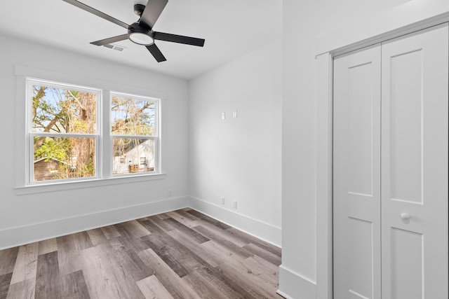 unfurnished bedroom featuring a closet, visible vents, ceiling fan, wood finished floors, and baseboards