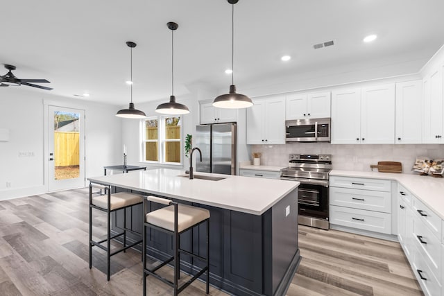 kitchen featuring visible vents, appliances with stainless steel finishes, a kitchen breakfast bar, a sink, and backsplash