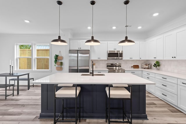 kitchen featuring stainless steel appliances, a sink, an island with sink, and decorative backsplash