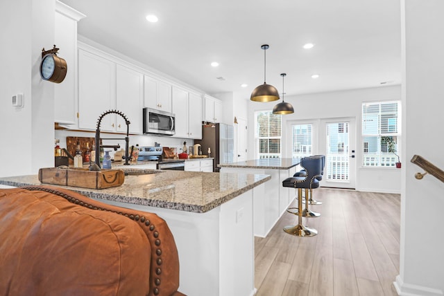 kitchen featuring pendant lighting, stainless steel appliances, white cabinetry, and stone countertops