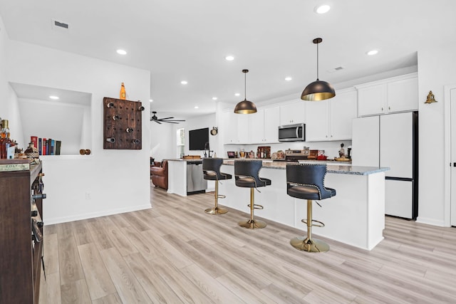 kitchen featuring appliances with stainless steel finishes, dark stone counters, ceiling fan, white cabinets, and hanging light fixtures