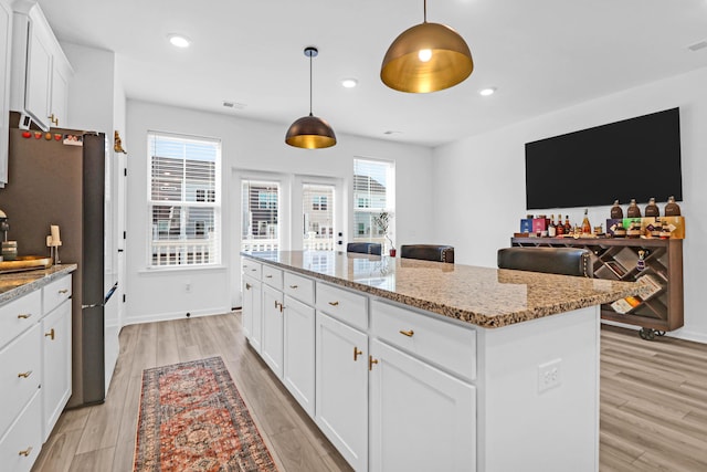 kitchen featuring a center island, light stone counters, white cabinetry, and hanging light fixtures