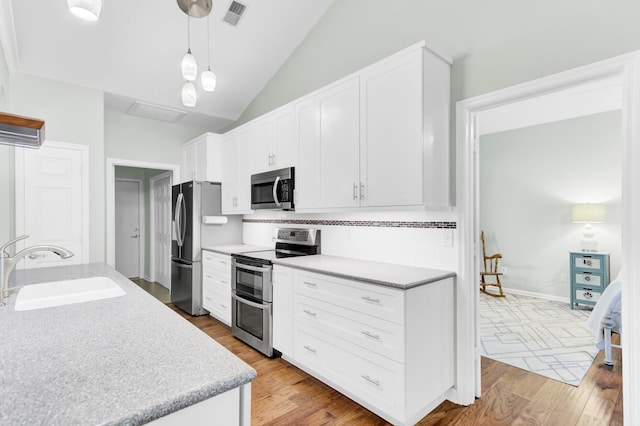 5406 Dwight Dr, North Charleston, SC 29420 - kitchen featuring appliances with stainless steel finishes, light wood finished floors, lofted ceiling, white cabinets, and hanging light fixtures