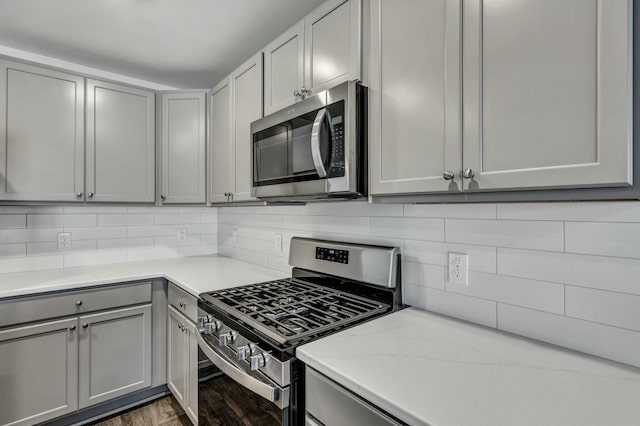 kitchen featuring tasteful backsplash, light countertops, gray cabinets, wood finished floors, and stainless steel appliances