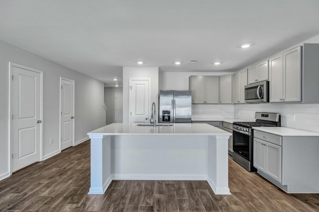 kitchen featuring a kitchen island with sink, dark wood-style flooring, a sink, gray cabinetry, and stainless steel appliances