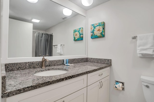 bathroom with vanity, toilet, a textured ceiling, and walk in shower