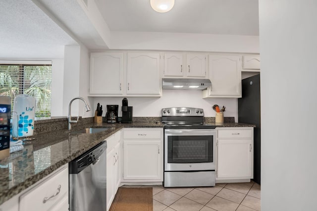 kitchen featuring sink, dark stone countertops, light tile patterned floors, appliances with stainless steel finishes, and white cabinets