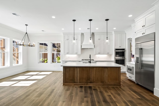 kitchen with dark wood-style flooring, custom exhaust hood, light countertops, visible vents, and built in appliances