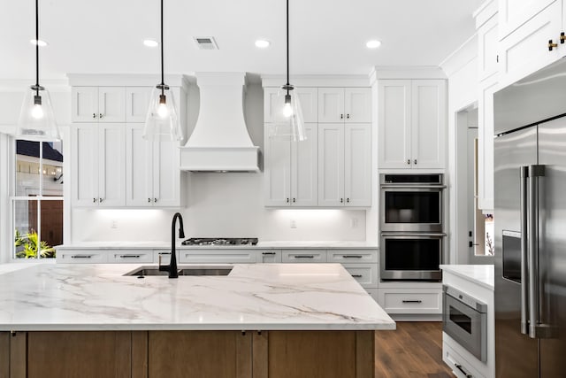 kitchen featuring custom range hood, visible vents, white cabinetry, a sink, and built in appliances