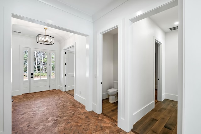 entryway with brick floor, crown molding, a notable chandelier, visible vents, and baseboards