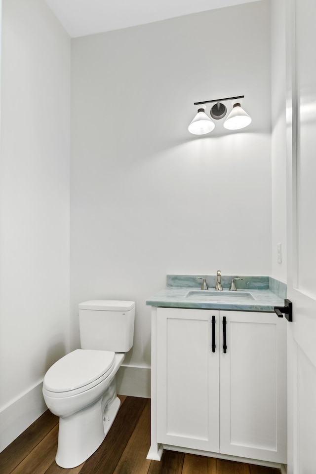 half bathroom featuring toilet, baseboards, wood finished floors, and vanity